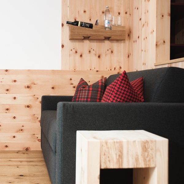 Sofa bed with red patterned pillows and a silent, electric-free minibar shelf in the Comfort Triple Room at Ski-Hotel Mondschein, Stuben am Arlberg, Austria – pine wood design with natural elegance