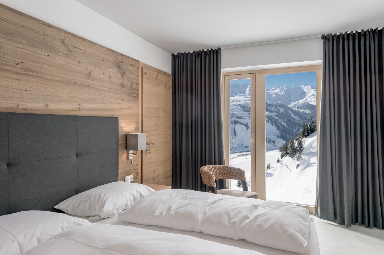 Private Double Room at Chalet Mondschein in Stuben am Arlberg, Austria – twin bed with wooden wall paneling, panoramic window, alpine view, and modern natural design