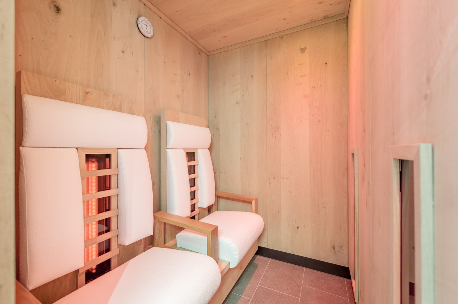 Infrared cabin in the Private SPA Suite Premium at Chalet Mondschein, Stuben am Arlberg – equipped with ergonomic wooden loungers, soft white upholstery, and gentle red light for deep muscle relaxation in an alpine wellness setting